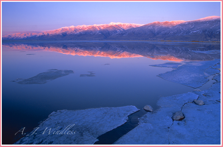 Sunset light illuminate the mountain ridges while sheets of ice break up around the perimeters of the Great Salt Lake.
