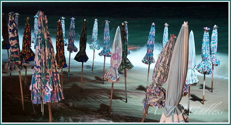 Late at night closed umbrellas present a pattern of color against the sea.