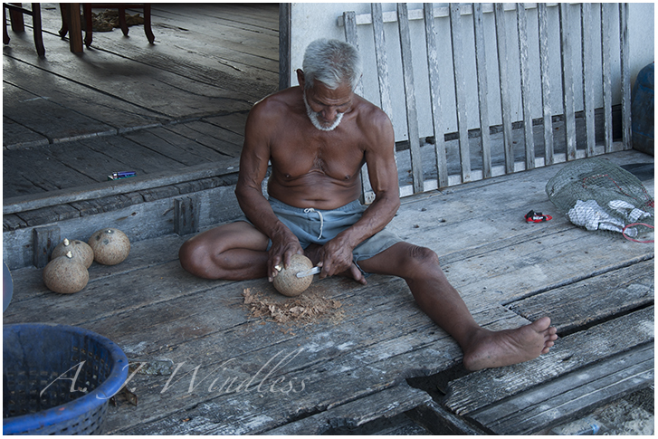 A Thai man sits on his porch husking coconuts