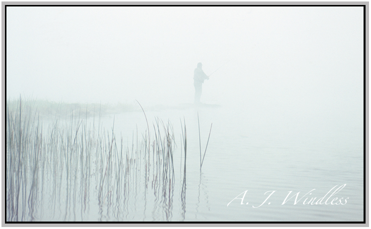 A fisherman nearly disappears in the fog while fishing on the point.
