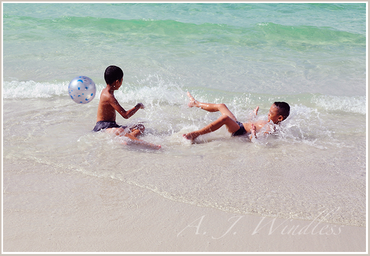 At the beach two Thai boys play ball in the water.