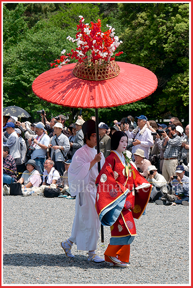 Escorted under an umbrella, this Japanese bride, dressed in traditional garments, marches in the Kyoto parade.