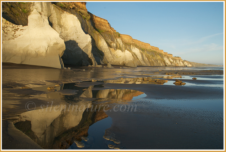 The receding tide leaves behind puddles that reflect the cliffs above.
