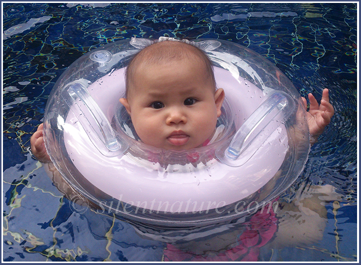 Small baby floating with her tube in a swimming pool.