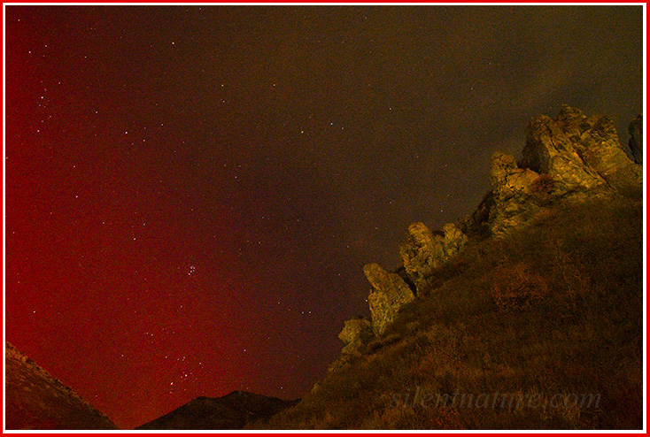 The northern lights put a red glow over the mountains near Ogden, while other lights set rock formations aglow.