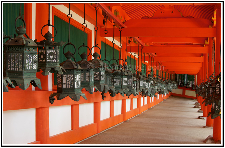 Ancient Japanese lanterns line up on both sides of a corrider of orange and white.