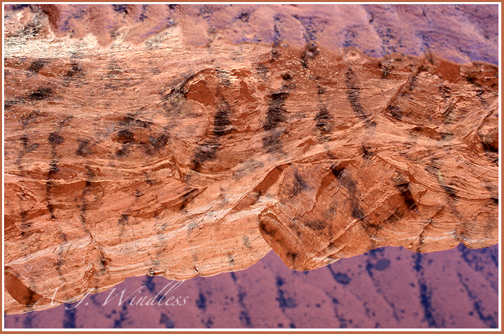 Reflections of majestic red rock formations in a puddle of water with a bottom of sand waves.
