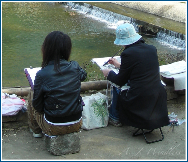 Two Chinese artists sit along the river and paint.