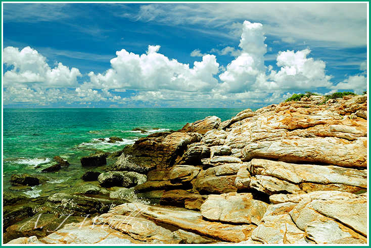 Dramatic clouds on the horizon meet dramatic rocks along the shoreline of a emerald green sea.