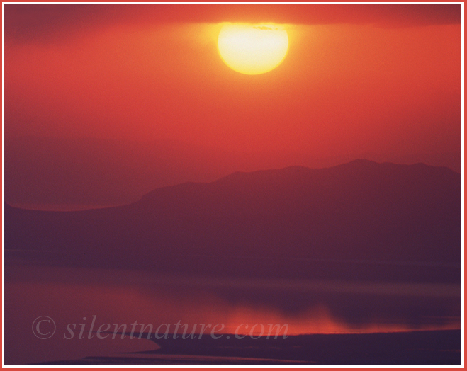 A late summer sun looms red and dark over the Great Salt Lake and Antelope Island.