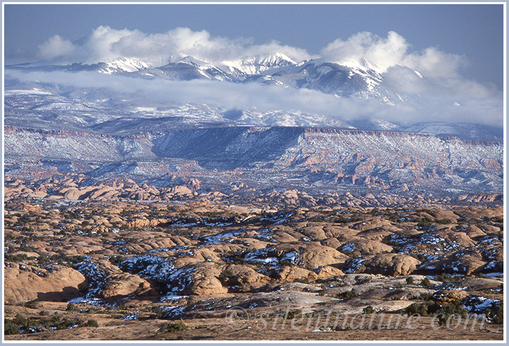 Light beige colored rocks form circular pattersn at the foot of snow topped La Sal Mountains.